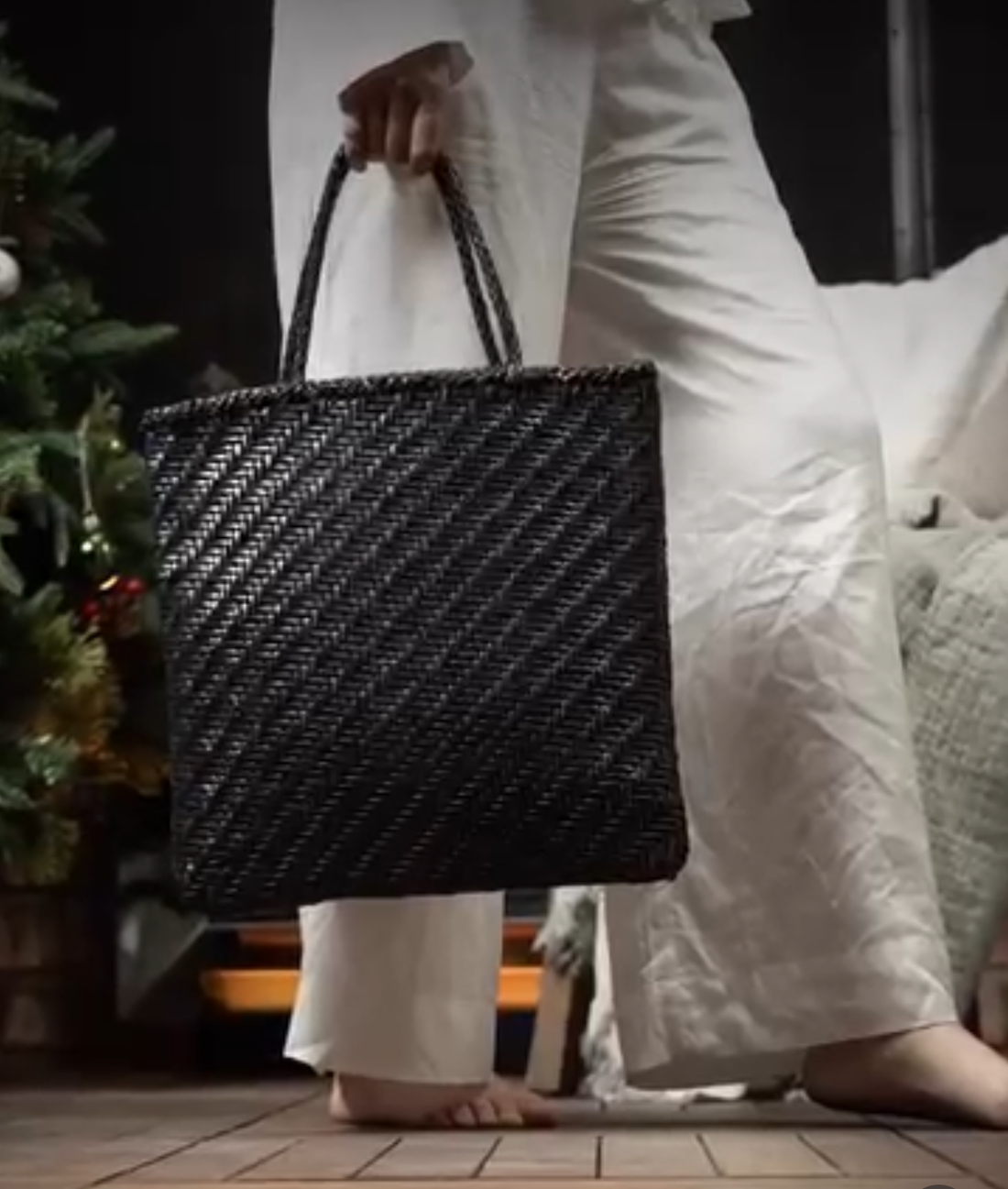 Person holding a black braided leather tote bag in a home setting