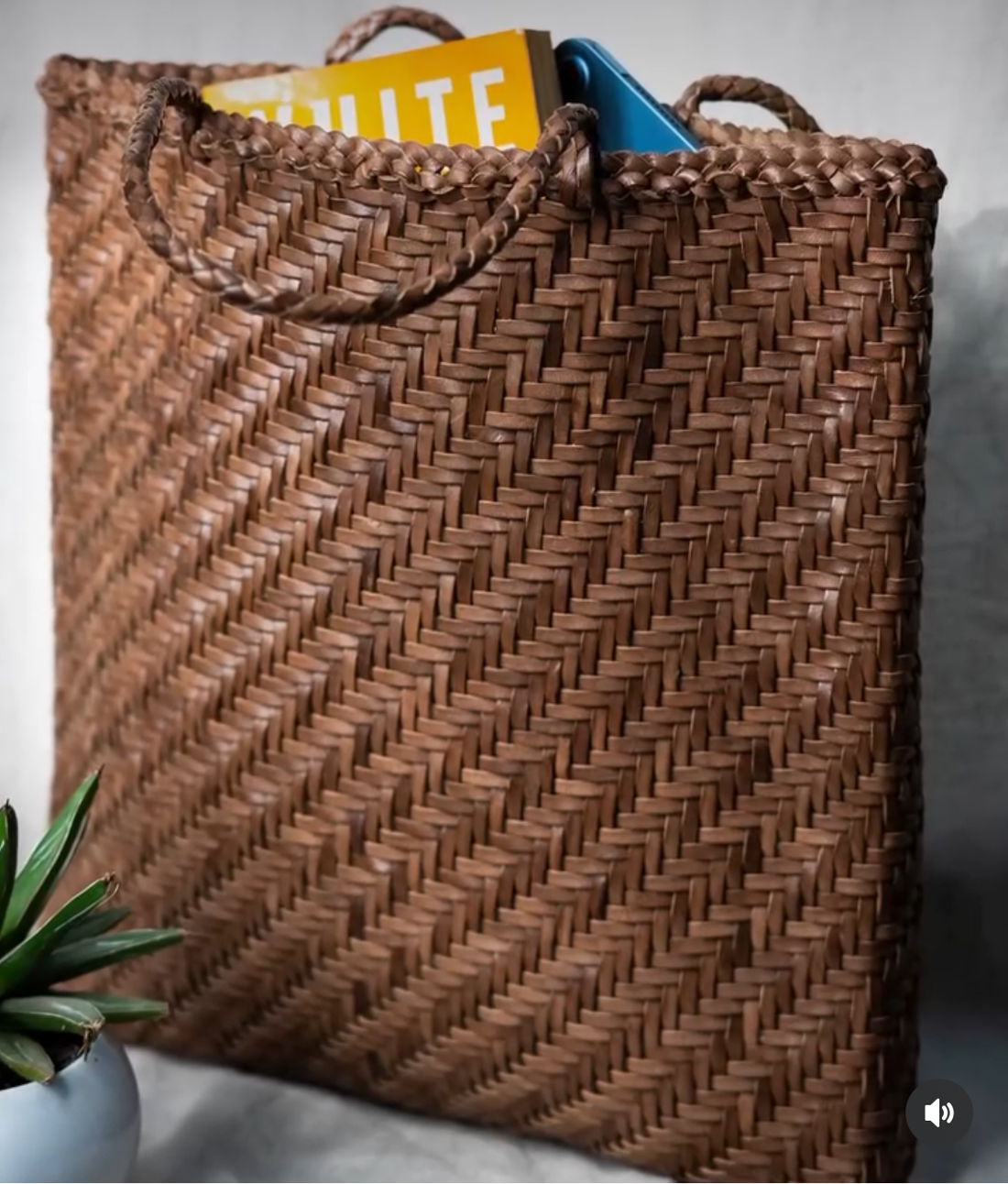 Woven brown braided leather tote bag with handles on a light gray background