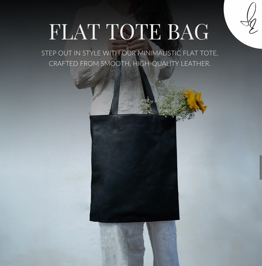 Black flat tote bag held by a person with flowers, on a plain background
