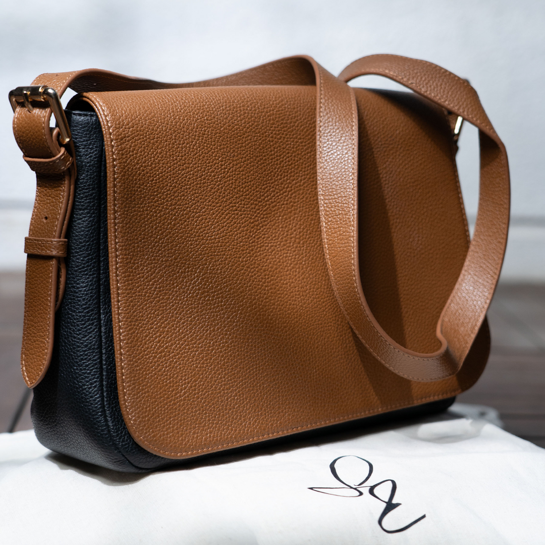 A black and brown genuine leather handbag with a zipper and flap closure, displayed against a neutral background.