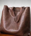 Brown leather tote bag on a wooden surface with a neutral background