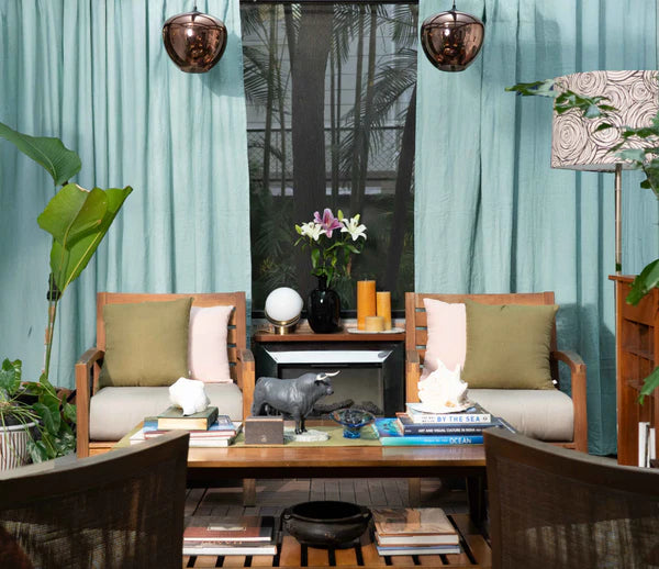 Modern living room with wooden chairs, a coffee table, and decorative items against a blue surd linen curtain.
