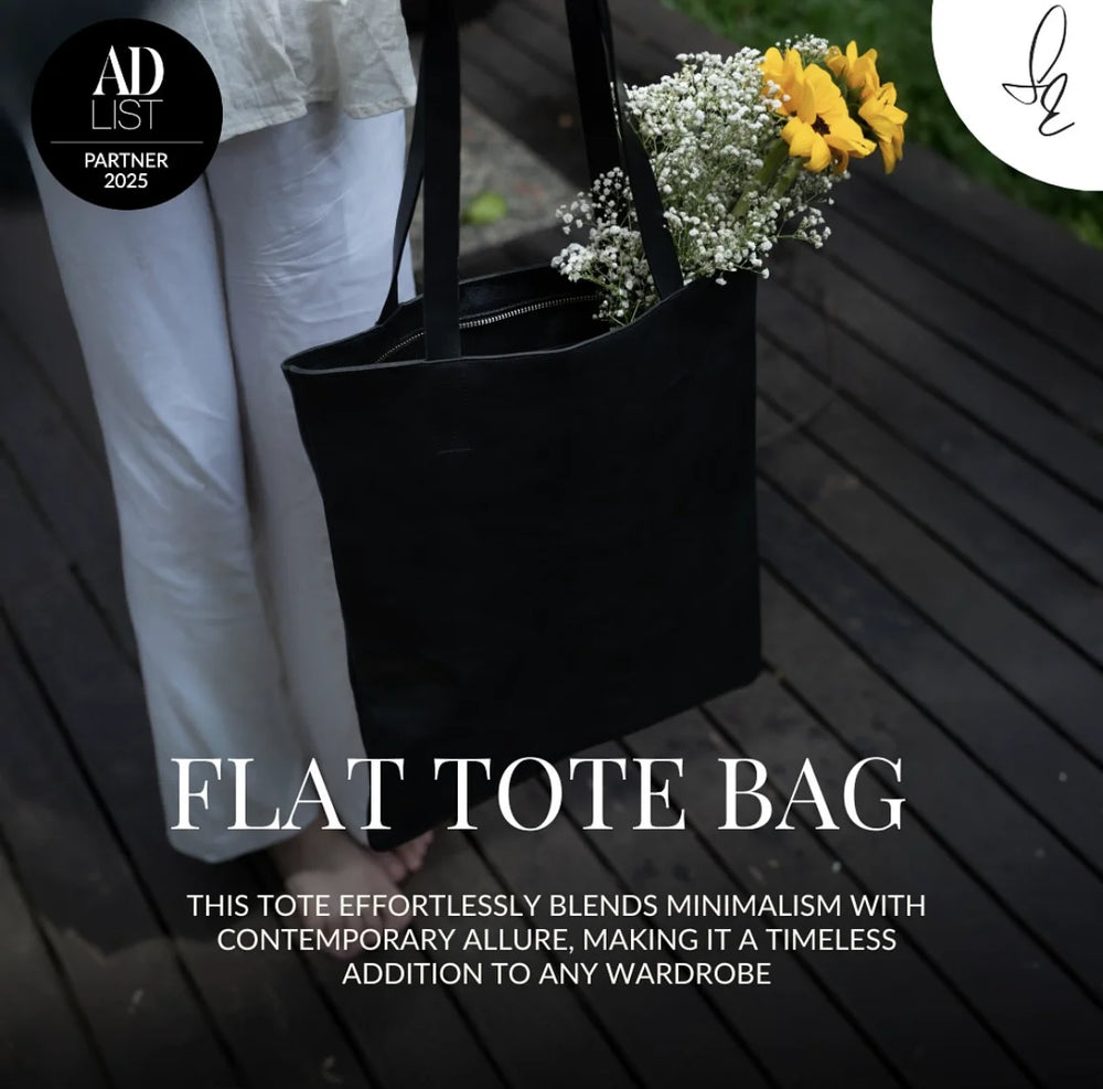 Black flat tote bag with flowers on a wooden surface, featuring text about the bag's design.