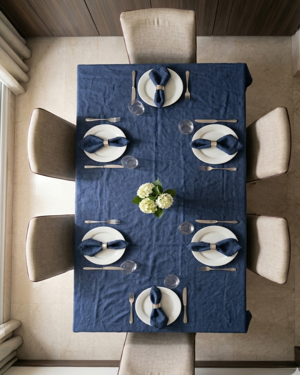 Dining table set with blue tablecloth, white plates, and silverware in a well-lit room.