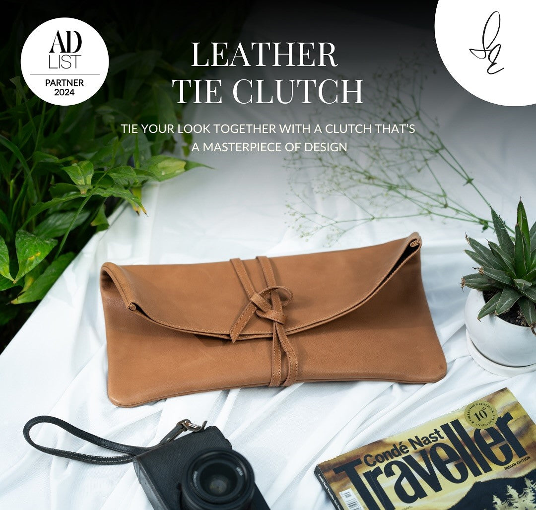 Brown leather tie clutch on a white surface with plants and a camera, featuring 'AD List' branding.