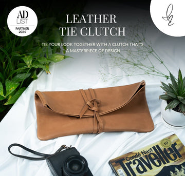 Brown leather tie clutch on a white surface with plants and a camera, featuring 'AD List' branding.
