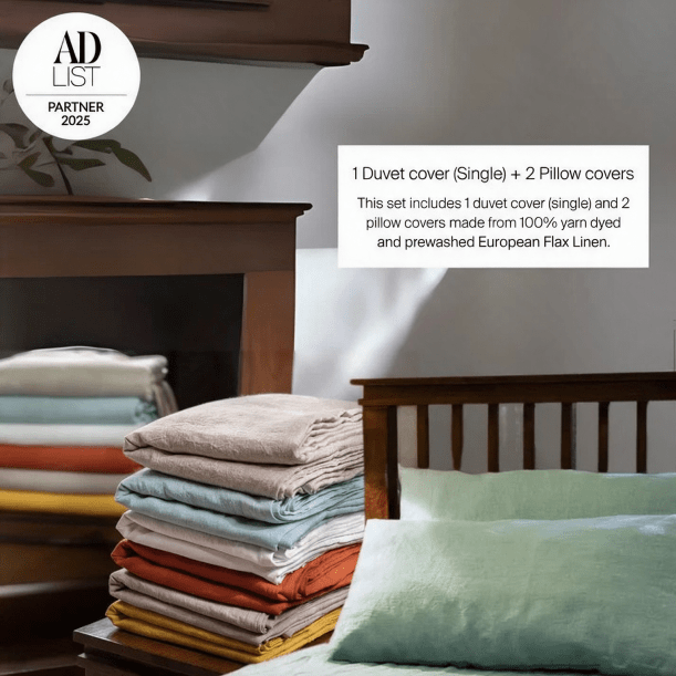 Stack of folded duvet covers and pillowcases with a bed and headboard in the background.