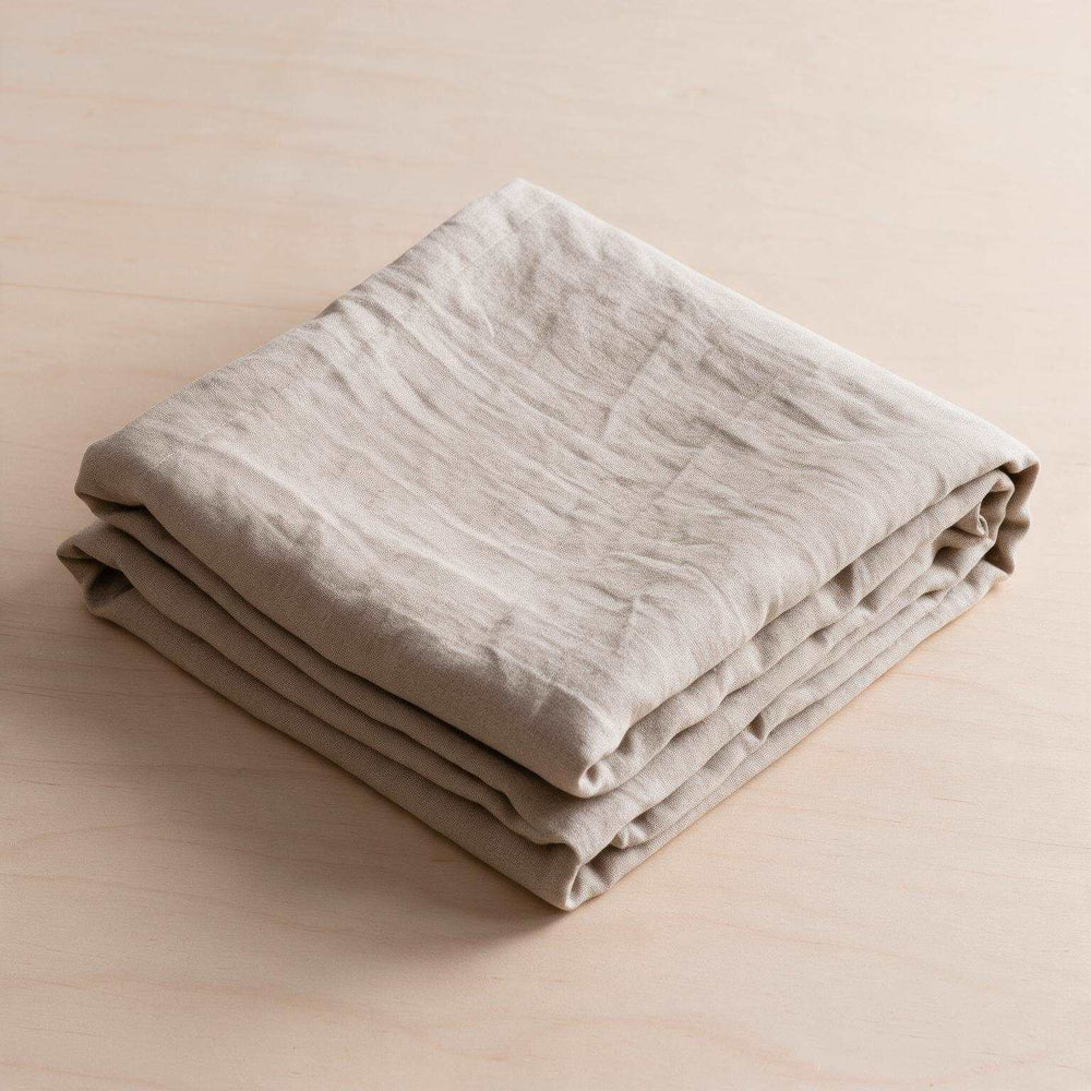 Close-up of two Natural Beige linen pillowcases on a matching flat sheet against a dark wood headboard, soft warm light highlighting the relaxed natural linen drape and texture