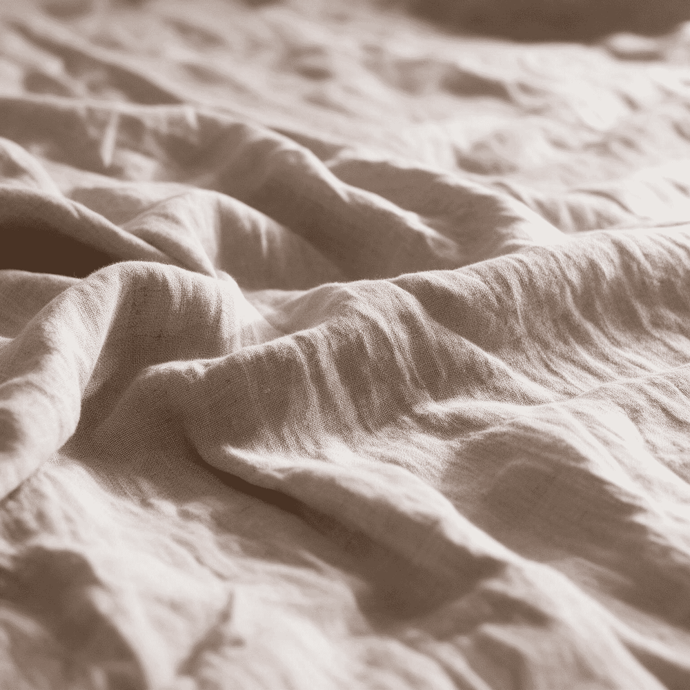 Macro close-up of Natural Beige linen flat sheet showing soft folds and natural linen weave texture in warm diffused light