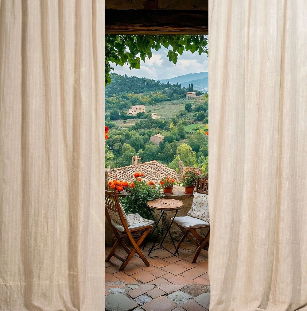 View from a balcony with curtains open, showing a scenic landscape with green hills and houses.
