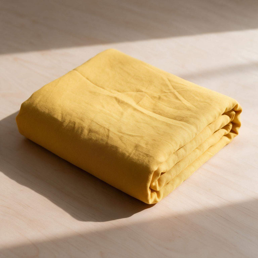 Nugget Gold linen flat sheet neatly folded on a neutral surface with diagonal window light casting soft shadows, showcasing the rich golden stonewashed linen texture⠋