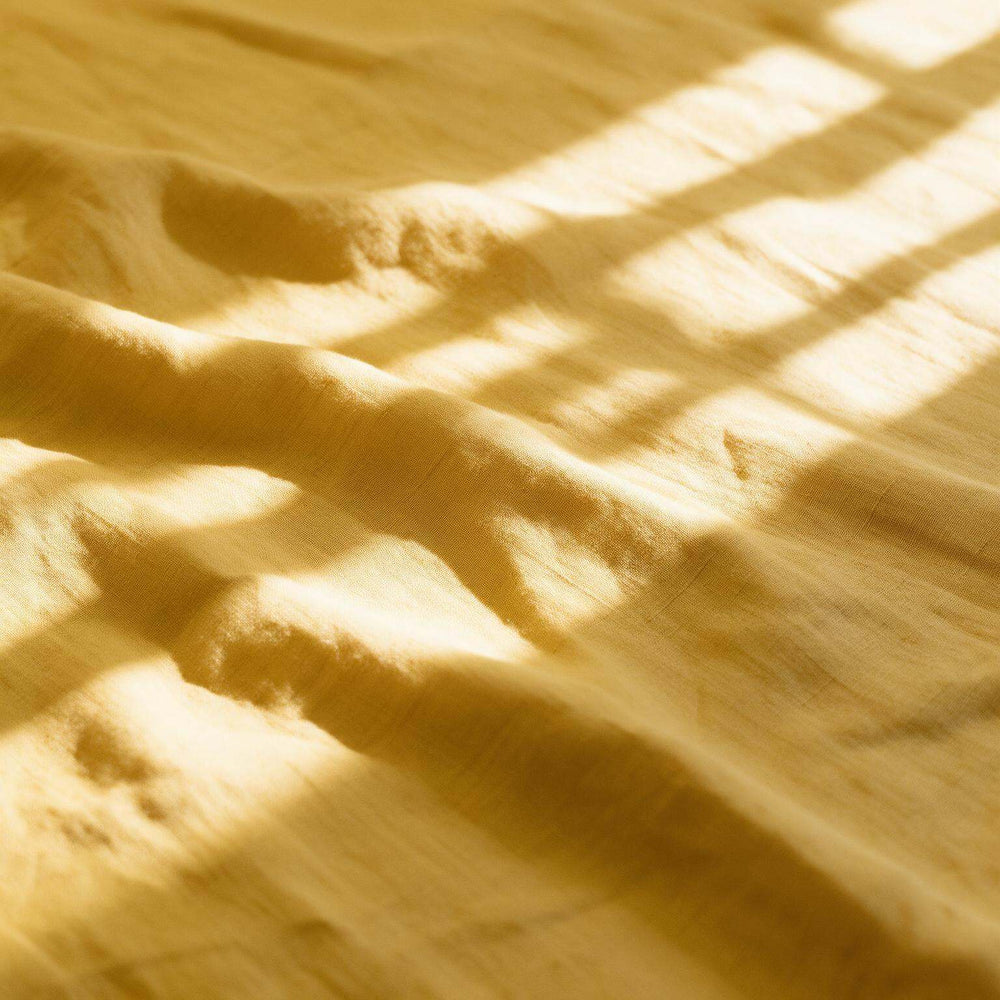 A close-up of draped yellow fabric with warm sunlight and window-blind style shadows cast across its surface.