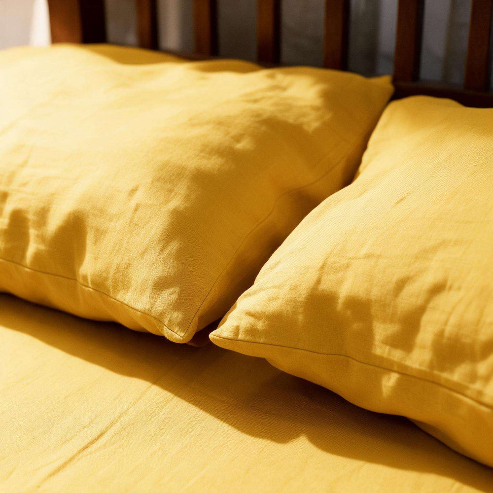 Two mustard yellow pillows resting on a matching yellow bedsheet, with a dark wooden headboard visible in the background.