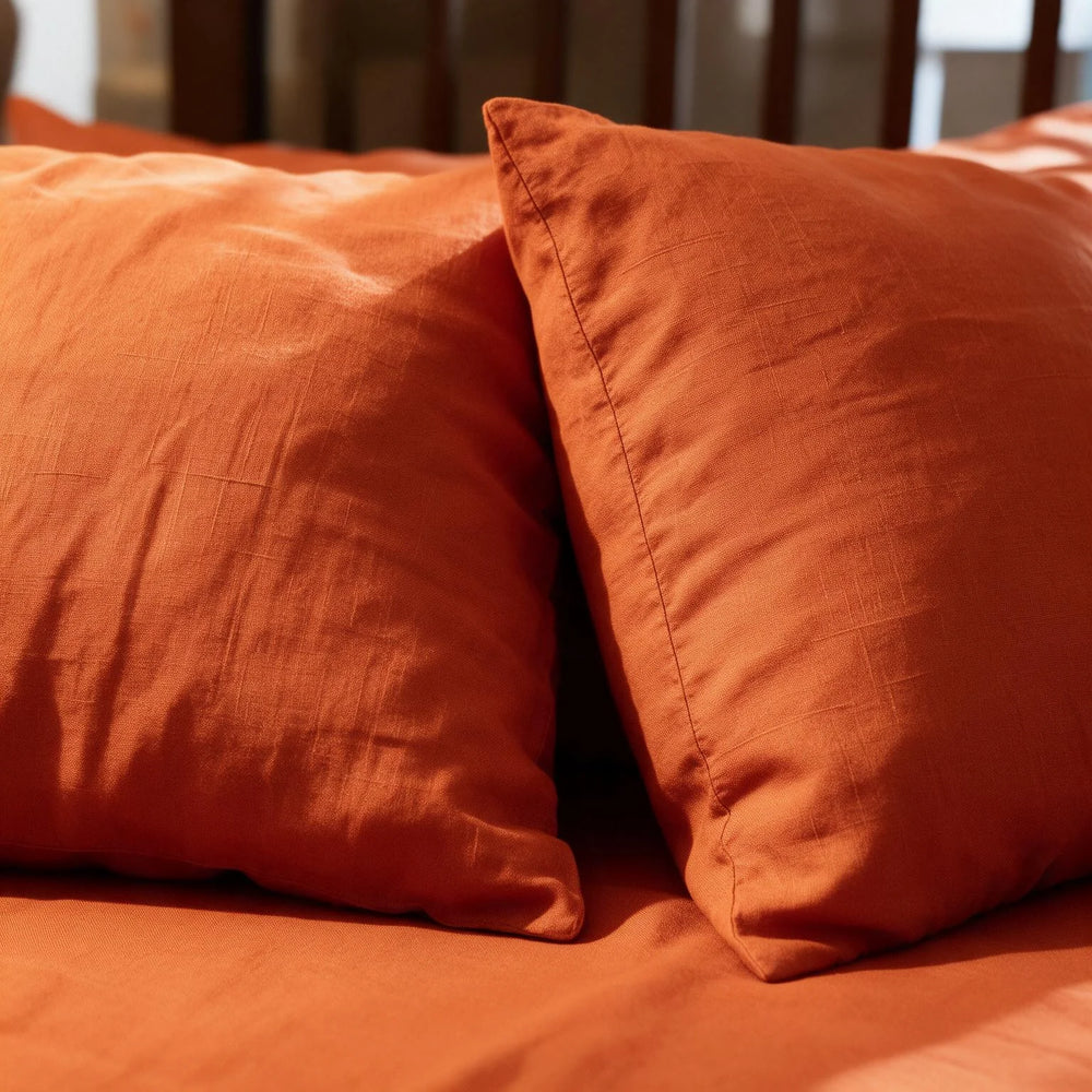 Close-up of two Rust Orange linen pillowcases resting on a matching flat sheet, showcasing the stonewashed terracotta linen weave in warm natural light