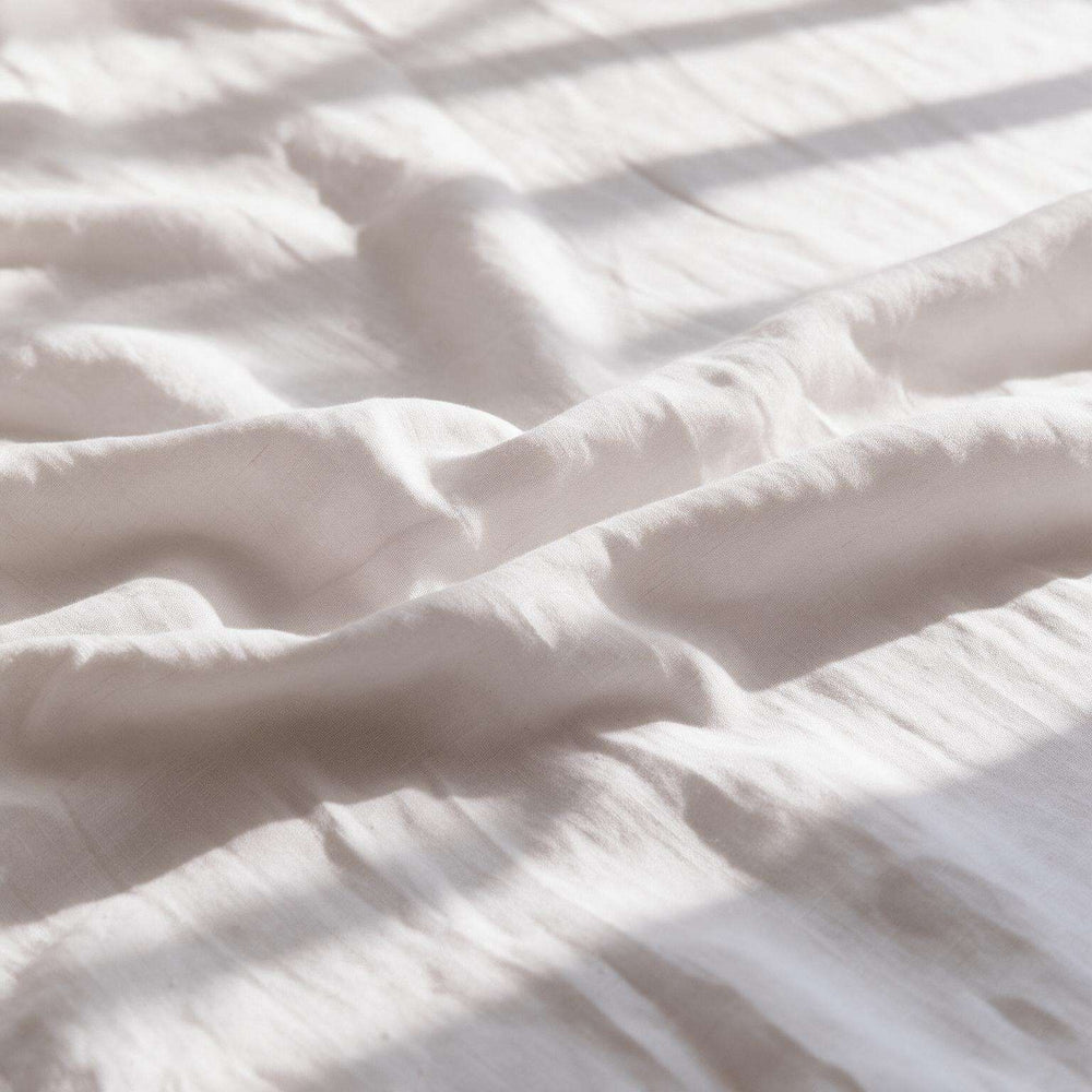 Flat lay of white linen flat sheet set — one folded flat sheet and two pillow covers laid on a light wood floor, showing the complete set contents