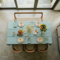 Dining table set with a light blue tablecloth, plates, and flowers in a well-lit room.