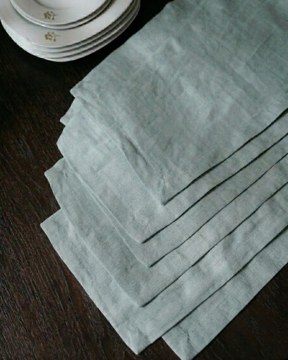 Set of light green napkins on a dark surface with plates in the background