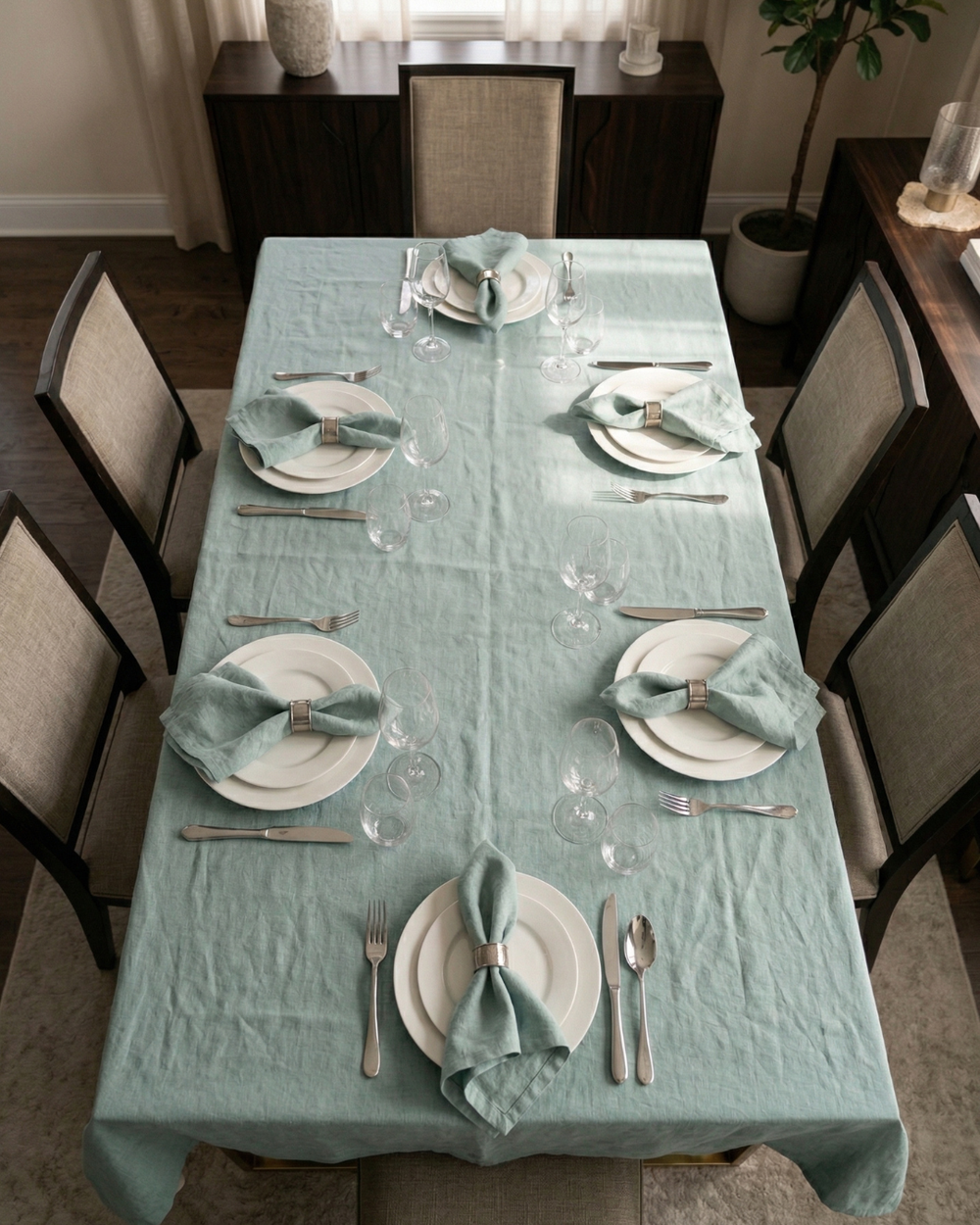 Dining table set with light blue tablecloth, plates, silverware, and napkins in a well-lit room.