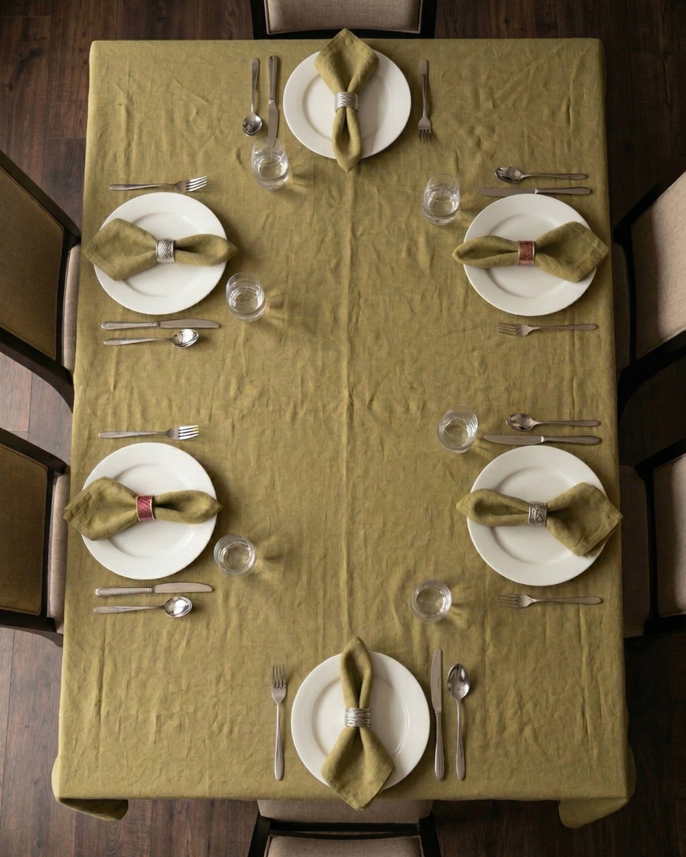 Dining table set with green napkins, white plates, and silverware on a green tablecloth.
