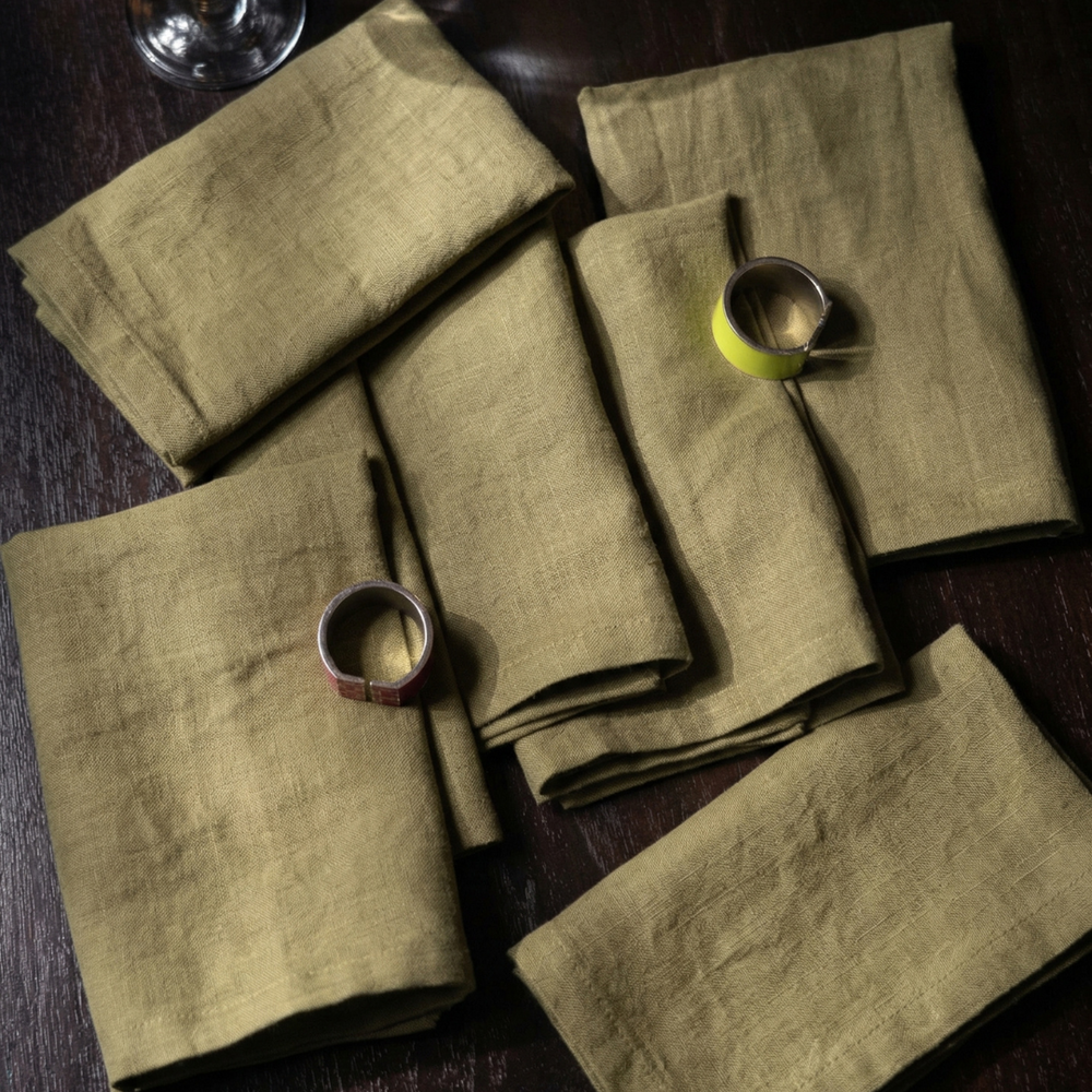 Set of green napkins on a dark surface with small metallic cups and a lime.