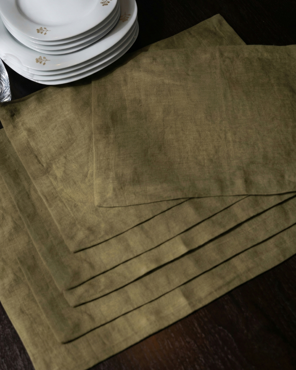 Set of green placemats on a dark surface with plates in the background.