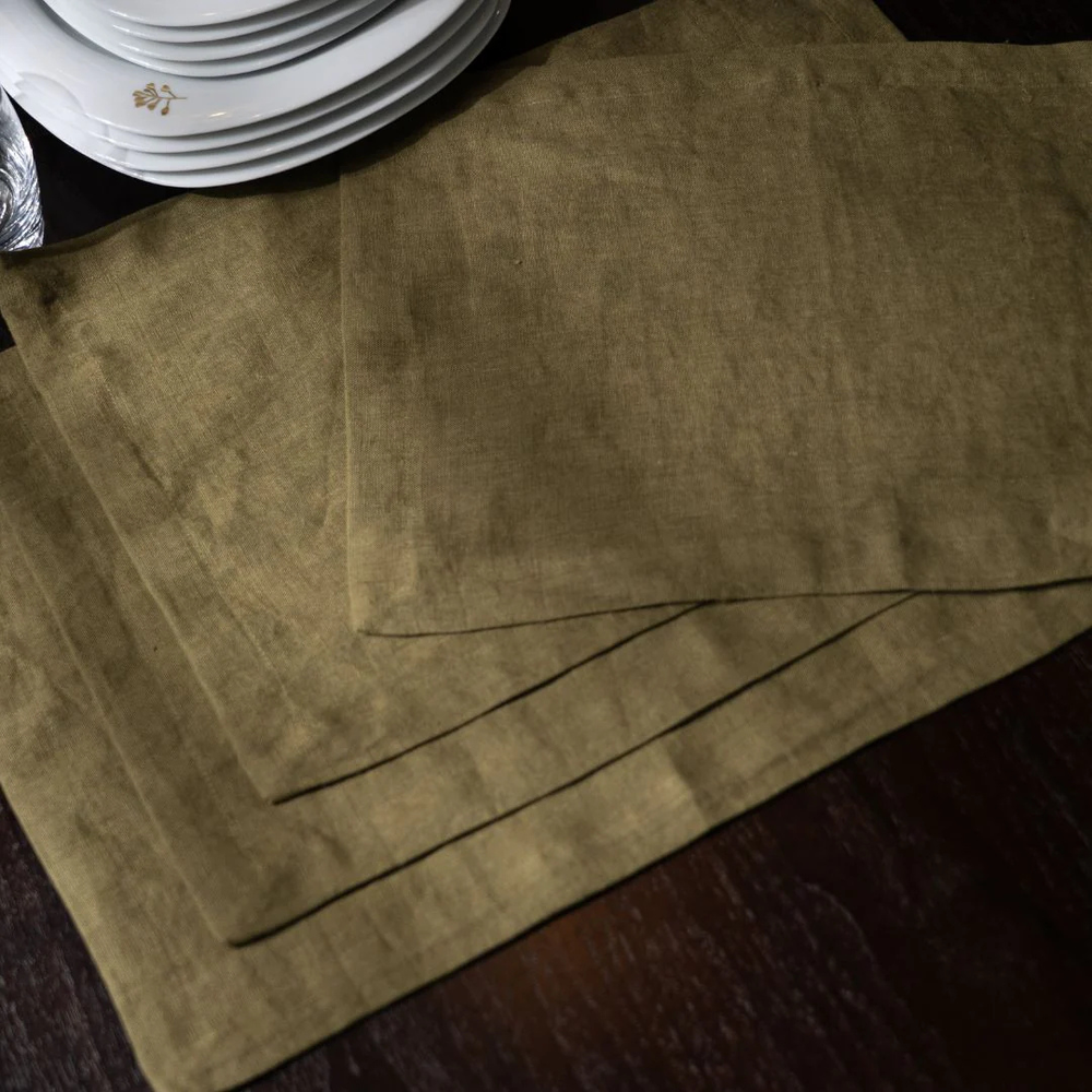 Set of brown placemats on a dark surface with white plates in the background.