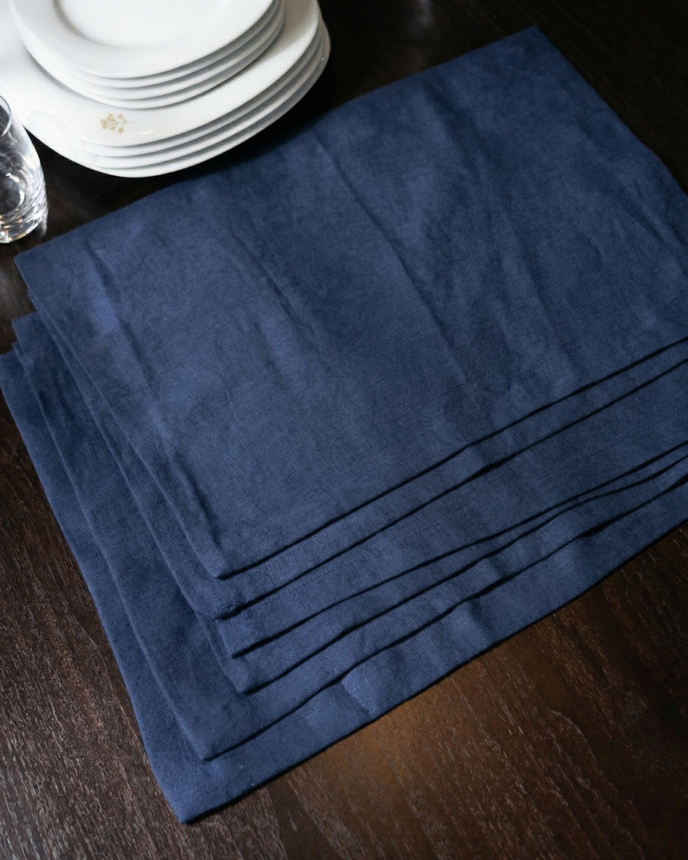 Set of blue placemats on a wooden table with white plates in the background.