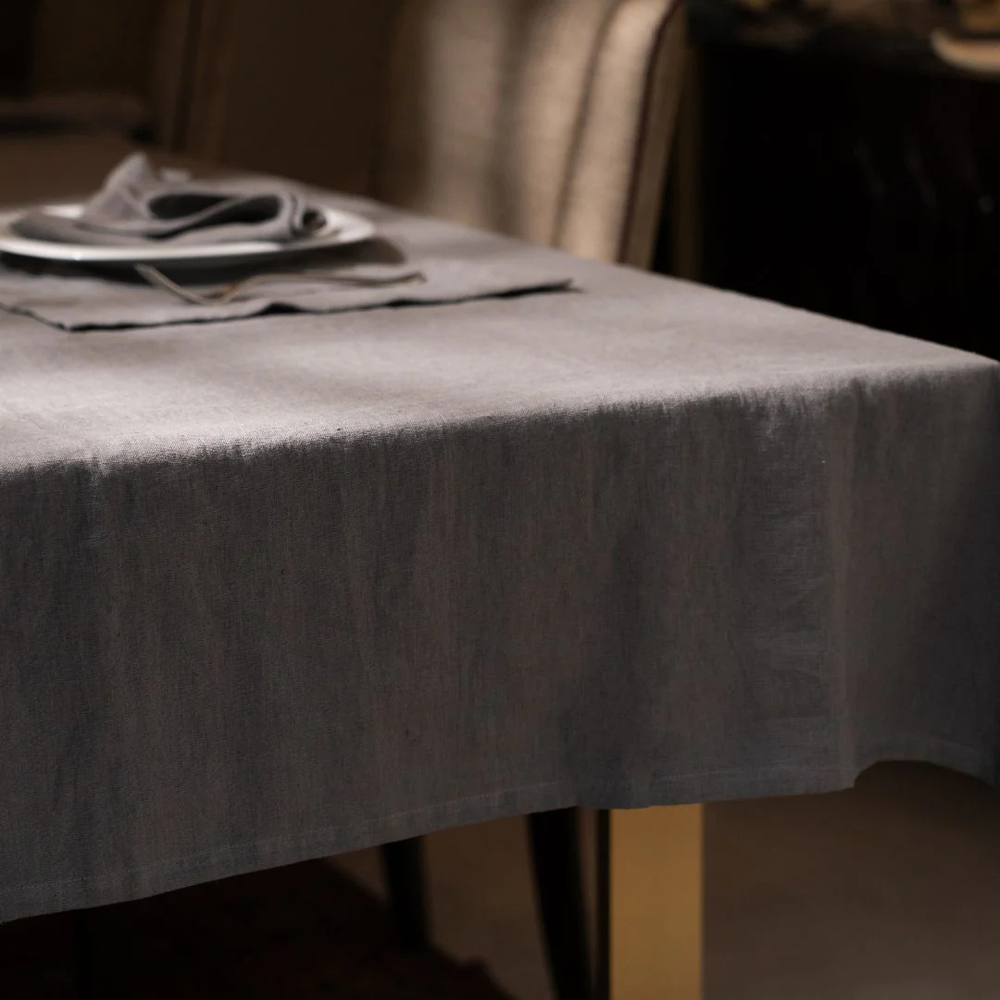 Gray tablecloth on a table with plates and napkins in a softly lit room.