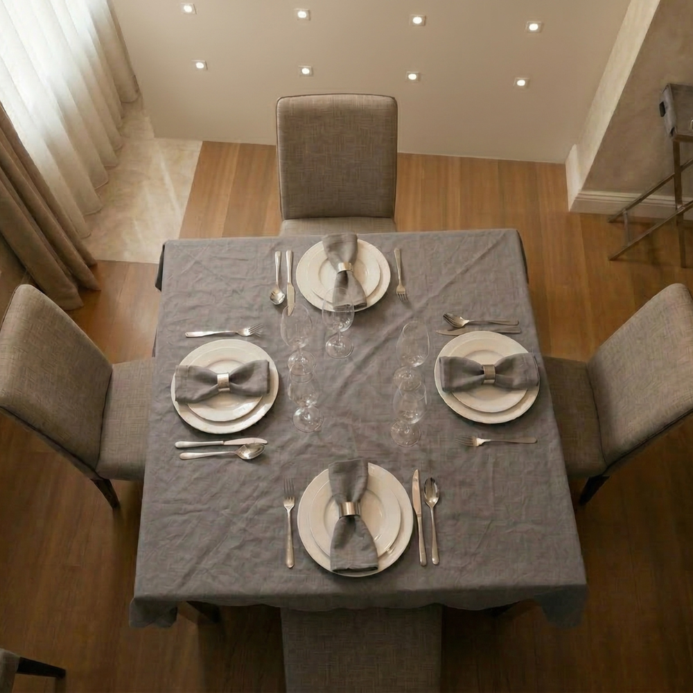 Dining table set with gray tablecloth, plates, and silverware in a well-lit room.