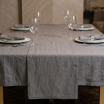 Dining table set with gray tablecloth, plates, glasses, and napkins.