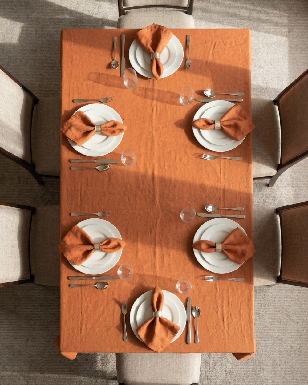 Dining table set with orange napkins and white plates in a room with chairs.