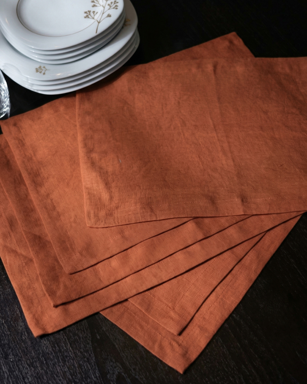 Set of brown placemats on a dark surface with white plates in the background.