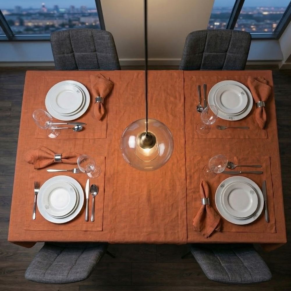 Dining table set for two with plates, silverware, and orange napkins, featuring a modern pendant light.