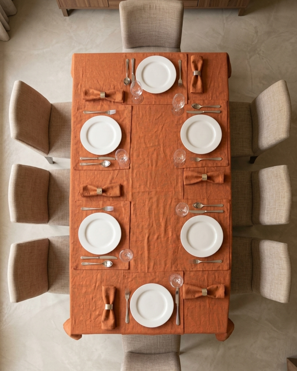 Dining table set with orange tablecloth, white plates, and silverware in a room.